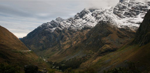 Big mountains with snow and a greener valley with a sliver of the road